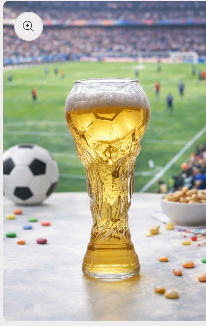Glass of beer with a soccer ball and snacks on a table in front of a soccer stadium.